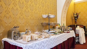 A buffet setup with various food items and a coffee station, set against a patterned wallpaper background.
