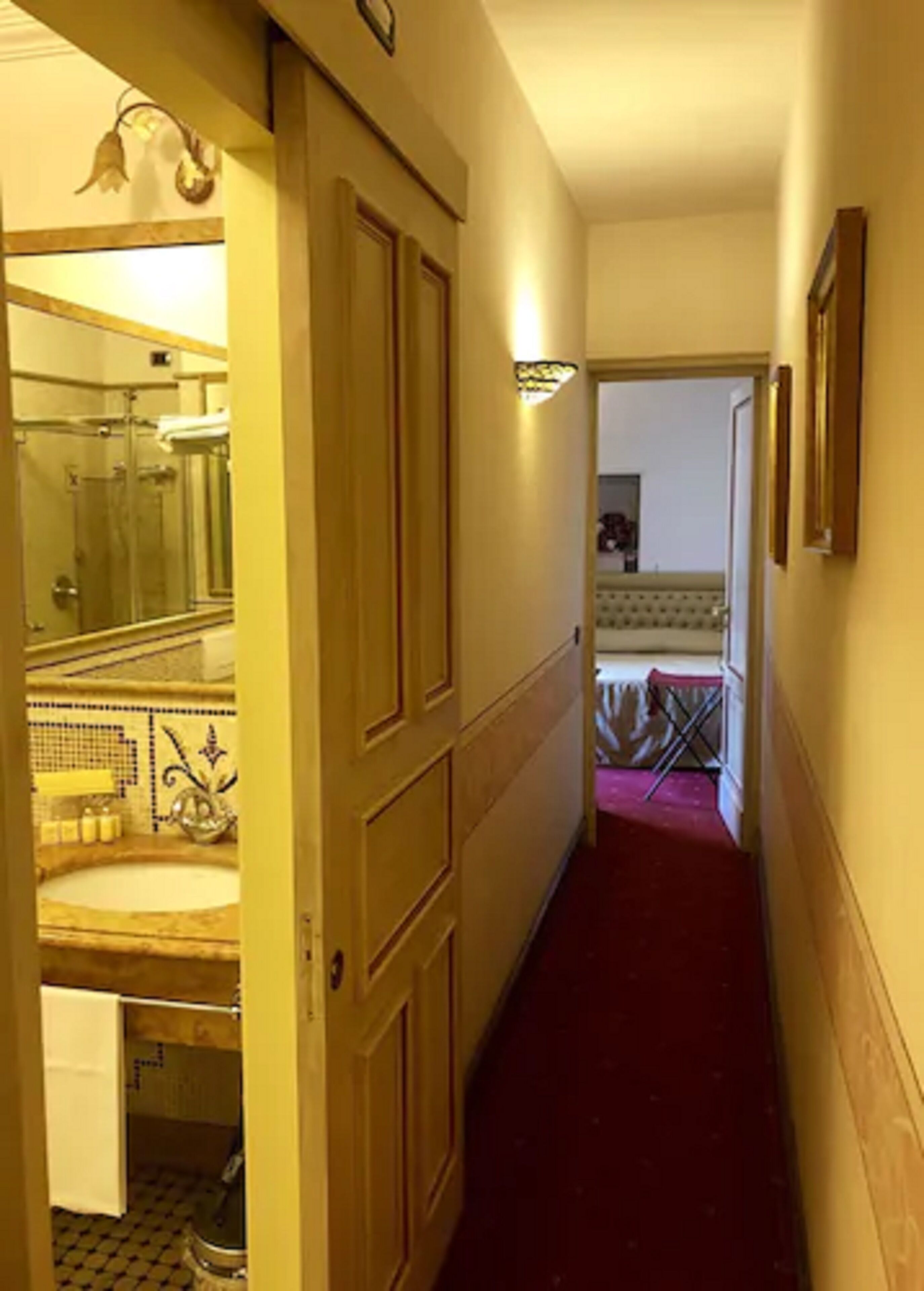 A hallway with a bathroom on the left, featuring a sink and mirror.