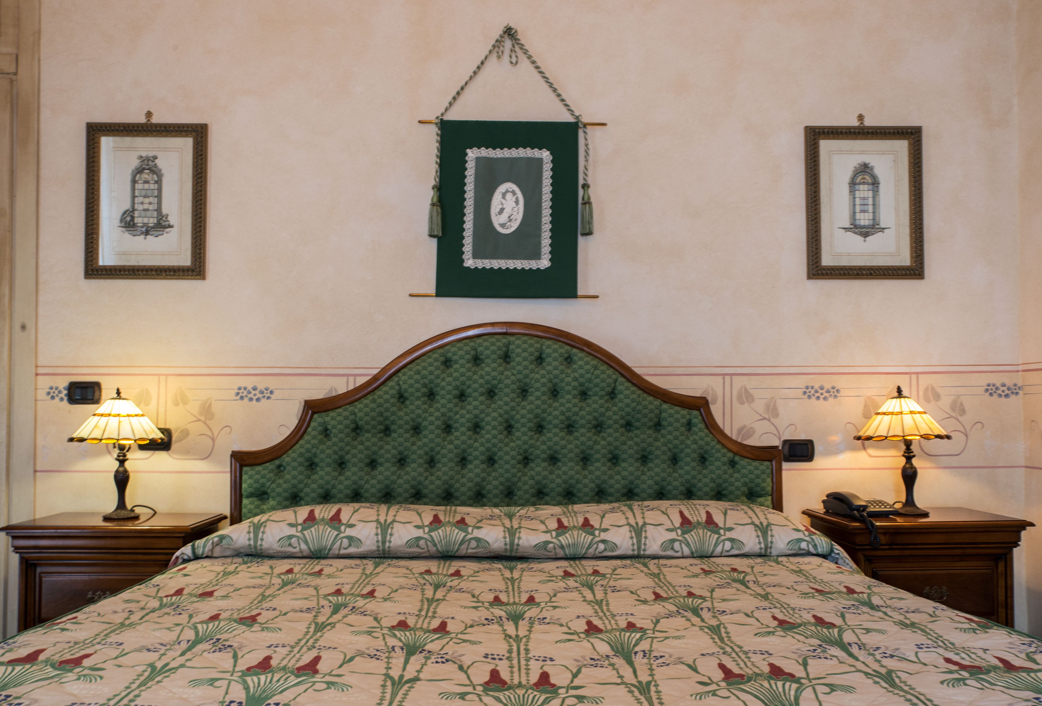 A neatly made bed with floral bedding, two bedside lamps, and framed pictures on the walls.