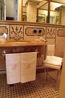 A bathroom with a tiled floor, a sink with a mirror above it, and a toilet with a towel hanging on the wall.
