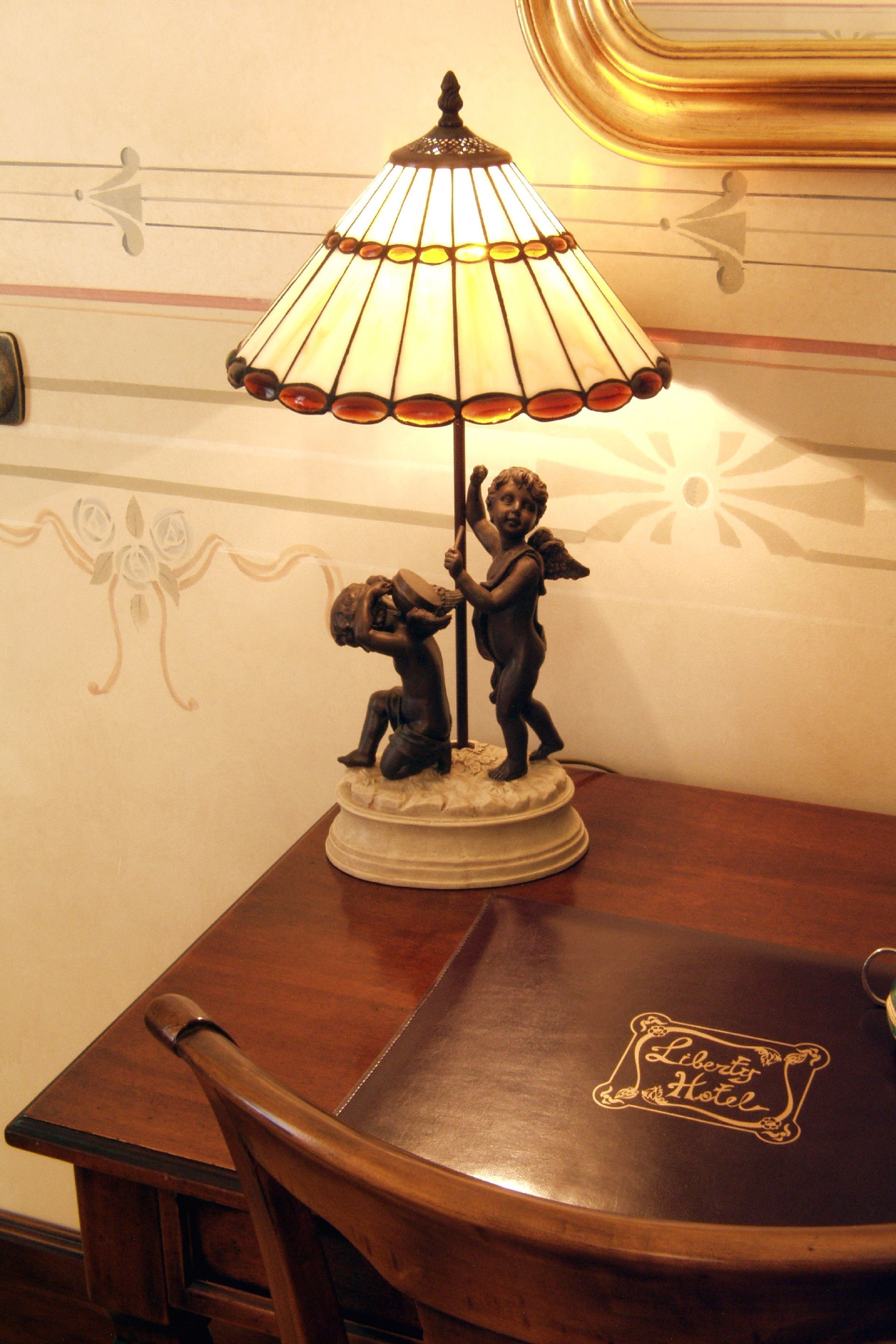 Une table ornée d’une lampe décorative surmontée d’une statuette d’un ange, une chaise en bois et une autre table portant une inscription avec le nom d’un hôtel.