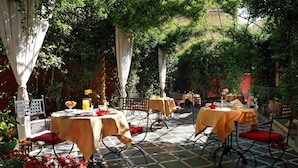 An outdoor patio with tables and chairs, surrounded by greenery and potted plants. - Liberty Hotel (Catania)