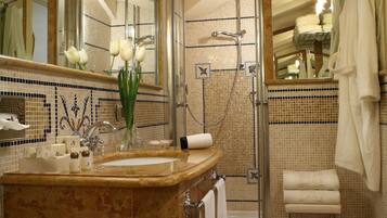 Un baño con un espejo grande, un lavabo con un florero y flores, una ducha y un perchero para toallas.