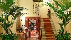 A grand staircase with ornate railings and a chandelier, flanked by large potted plants. - Liberty Hotel (Catania)