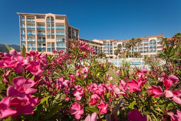 A hotel with multiple balconies, a pool area, and lush pink flowers in the foreground.