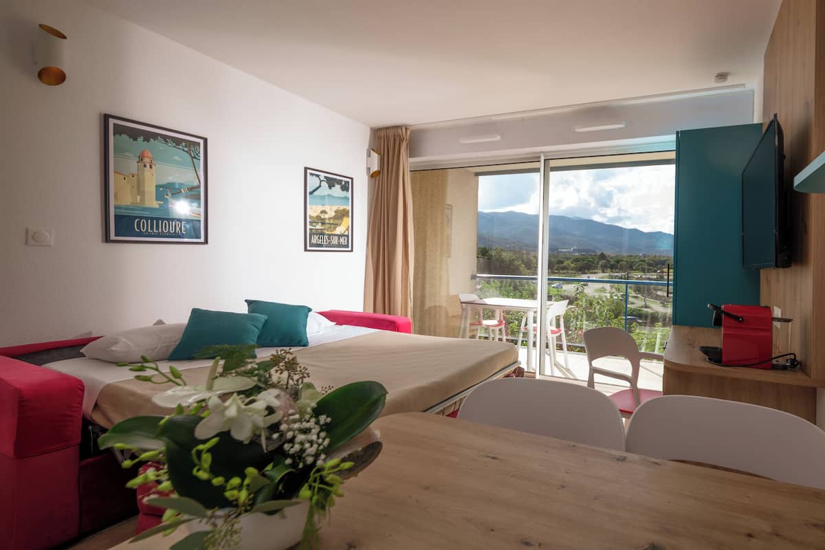 Ein Hotelzimmer mit Bett, Esstisch, Stühlen, Fernseher und einem Balkon mit Blick.