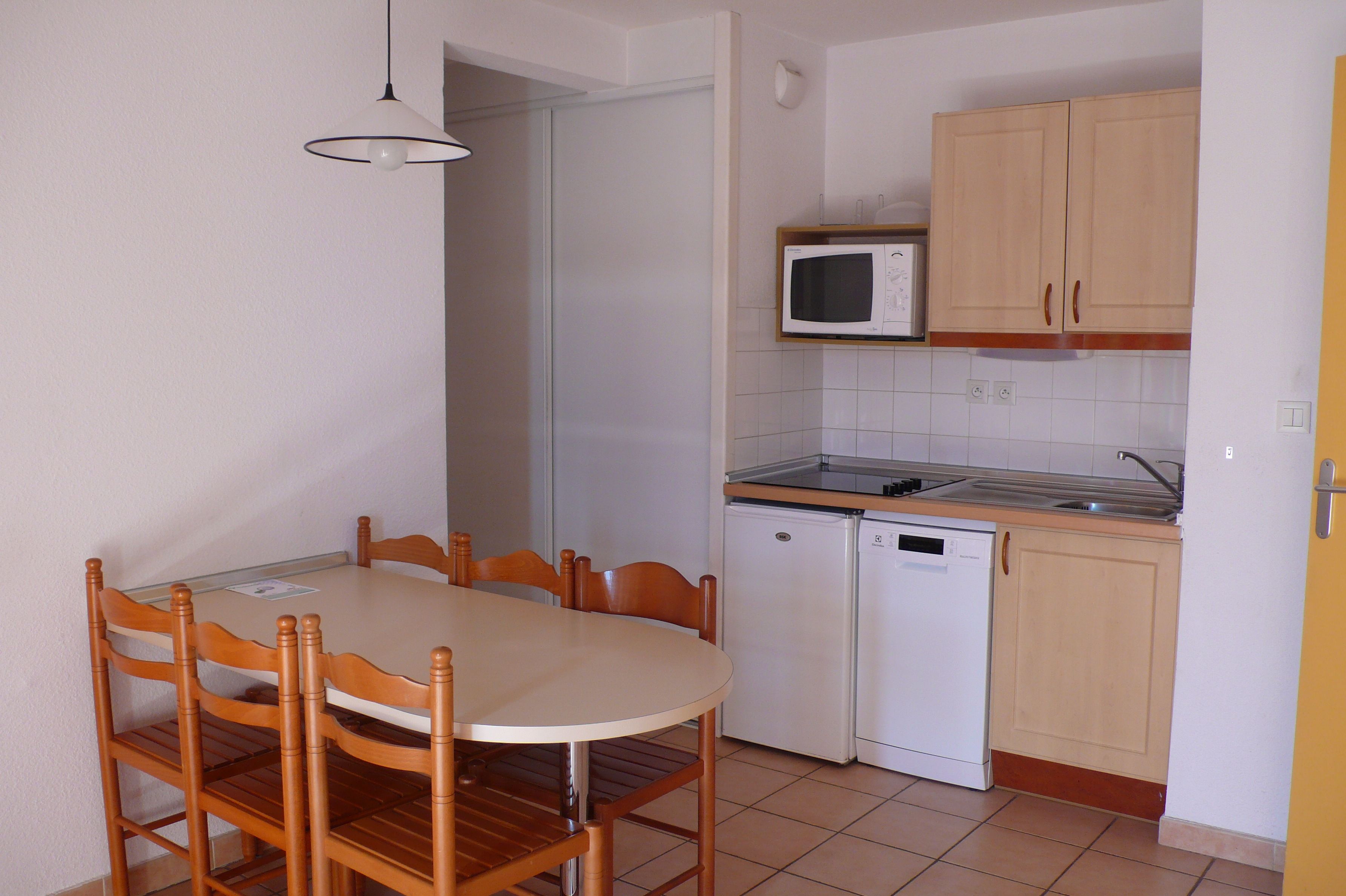 A compact kitchen with a dining table, chairs, a microwave, a dishwasher, and wooden cabinets.
