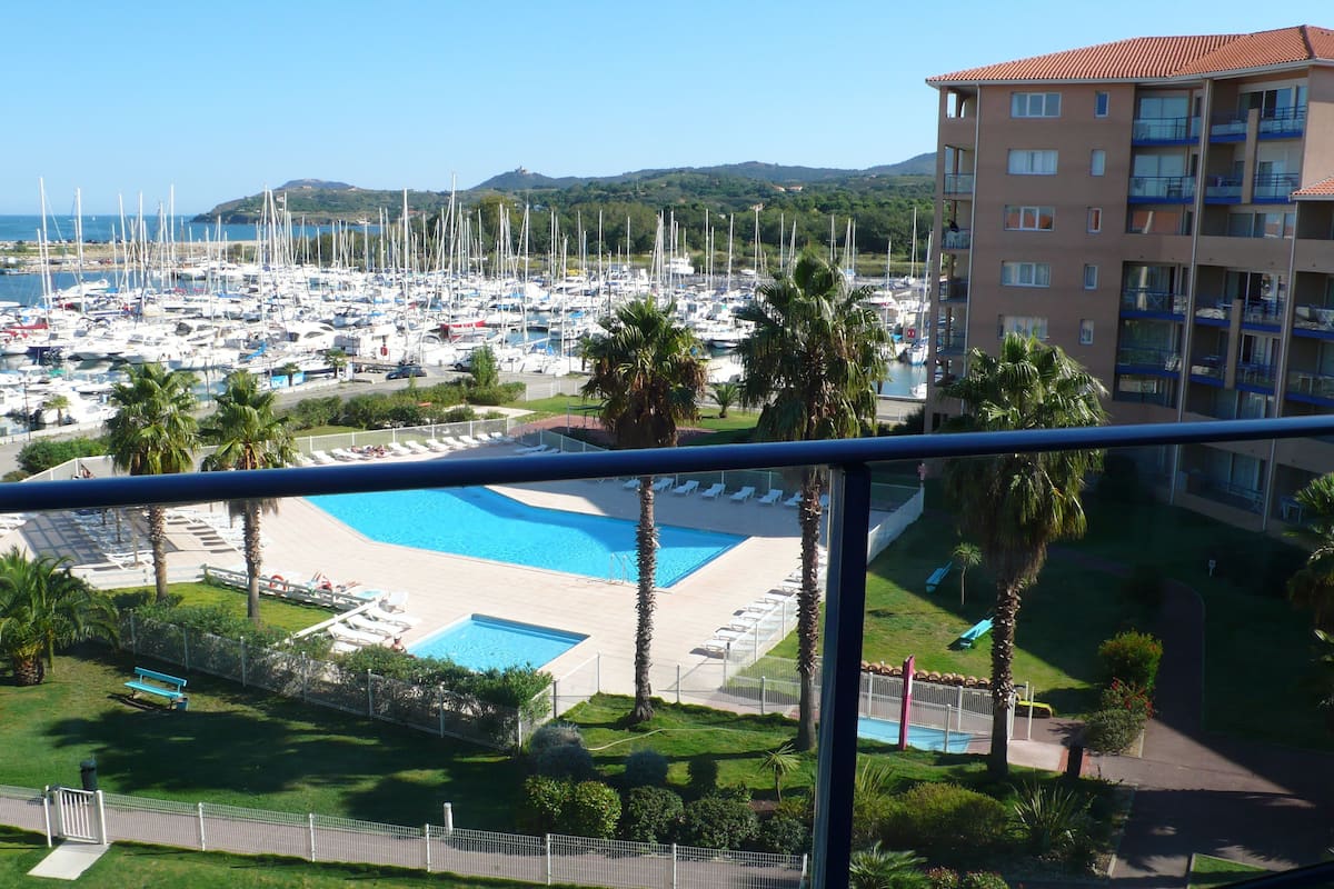 Ein Yachthafen mit zahlreichen Booten, einem Schwimmbad und einem Hotelgebäude mit Balkonen.