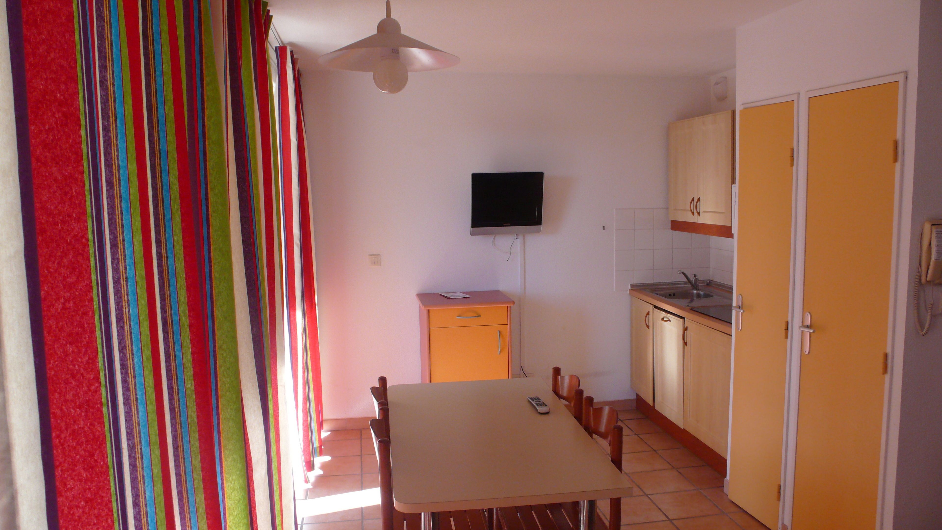 Una cocina compacta con una mesa de comedor, sillas, un televisor montado en la pared y un teléfono.