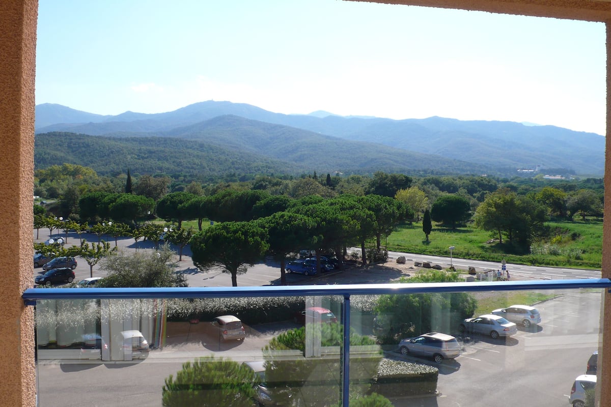 Blick aus einem Fenster auf einen Parkplatz mit Autos, Bäumen und entfernte Berge.