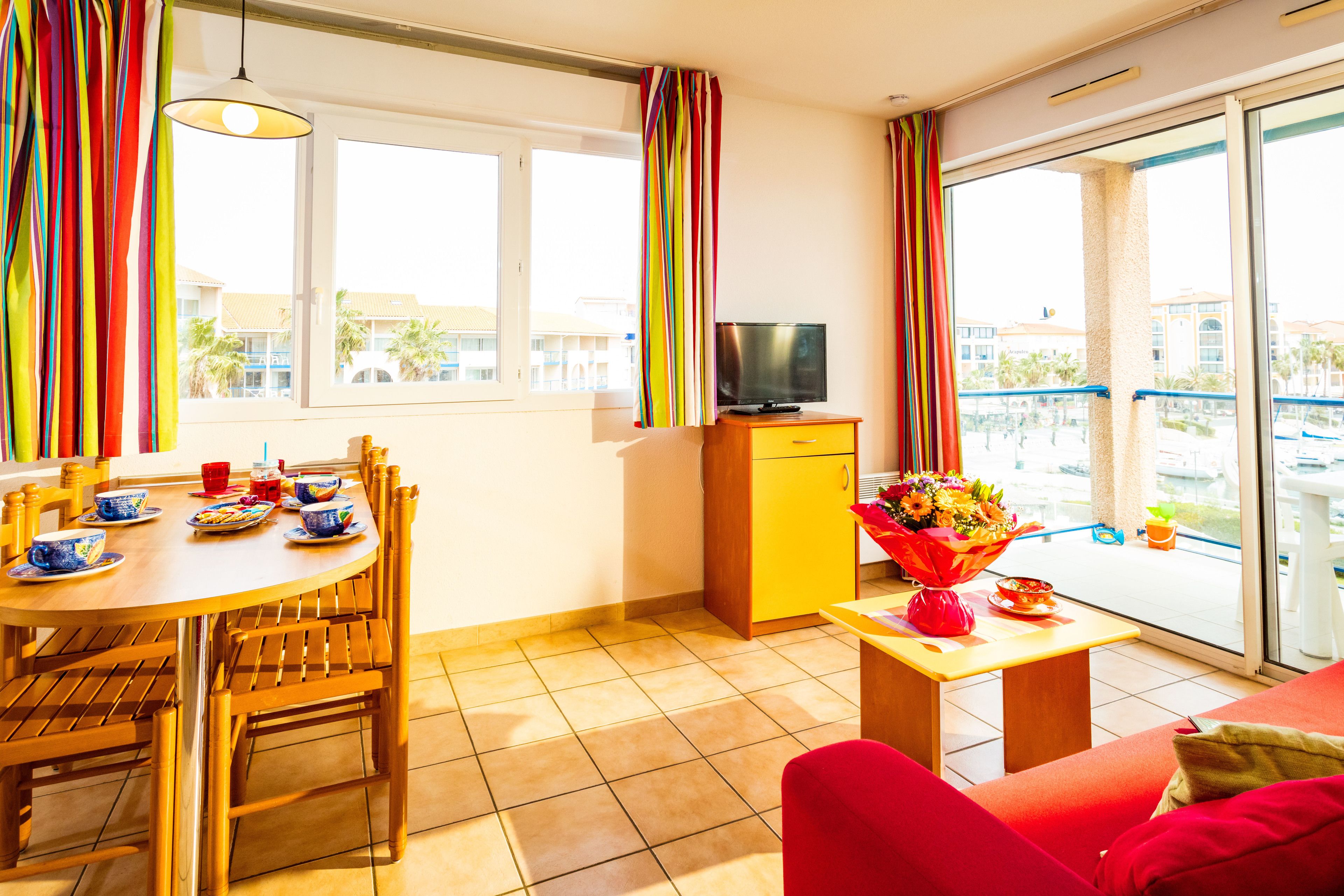Una sala moderna con comedor, televisor y balcón con vistas a edificios.