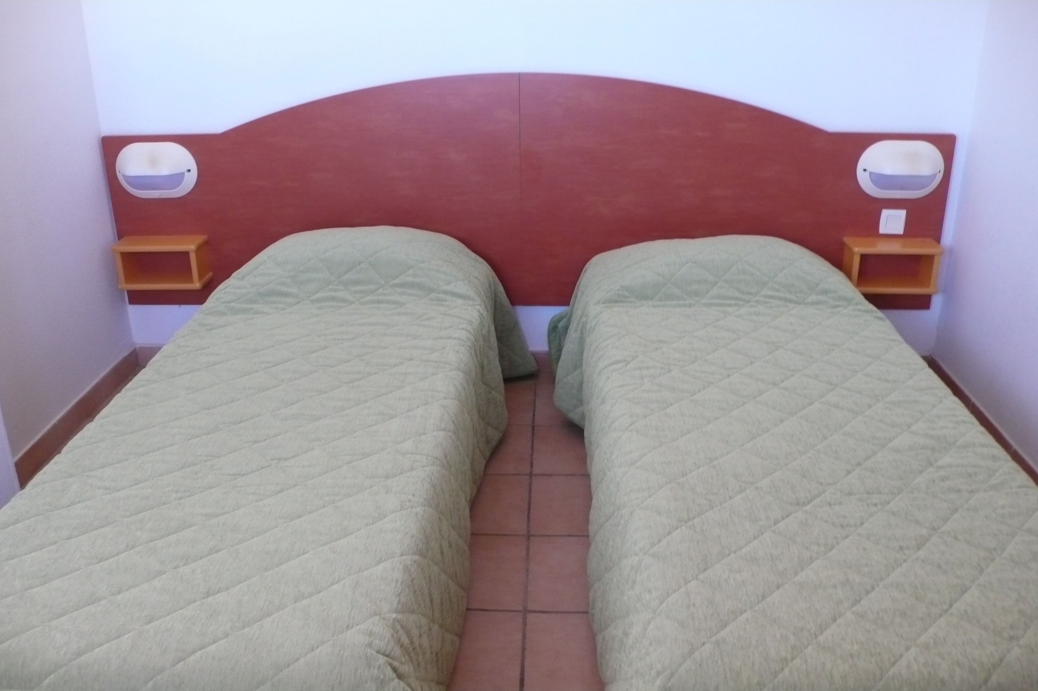Habitación doble con dos camas individuales, cabecera roja y mesitas de noche con lámparas.