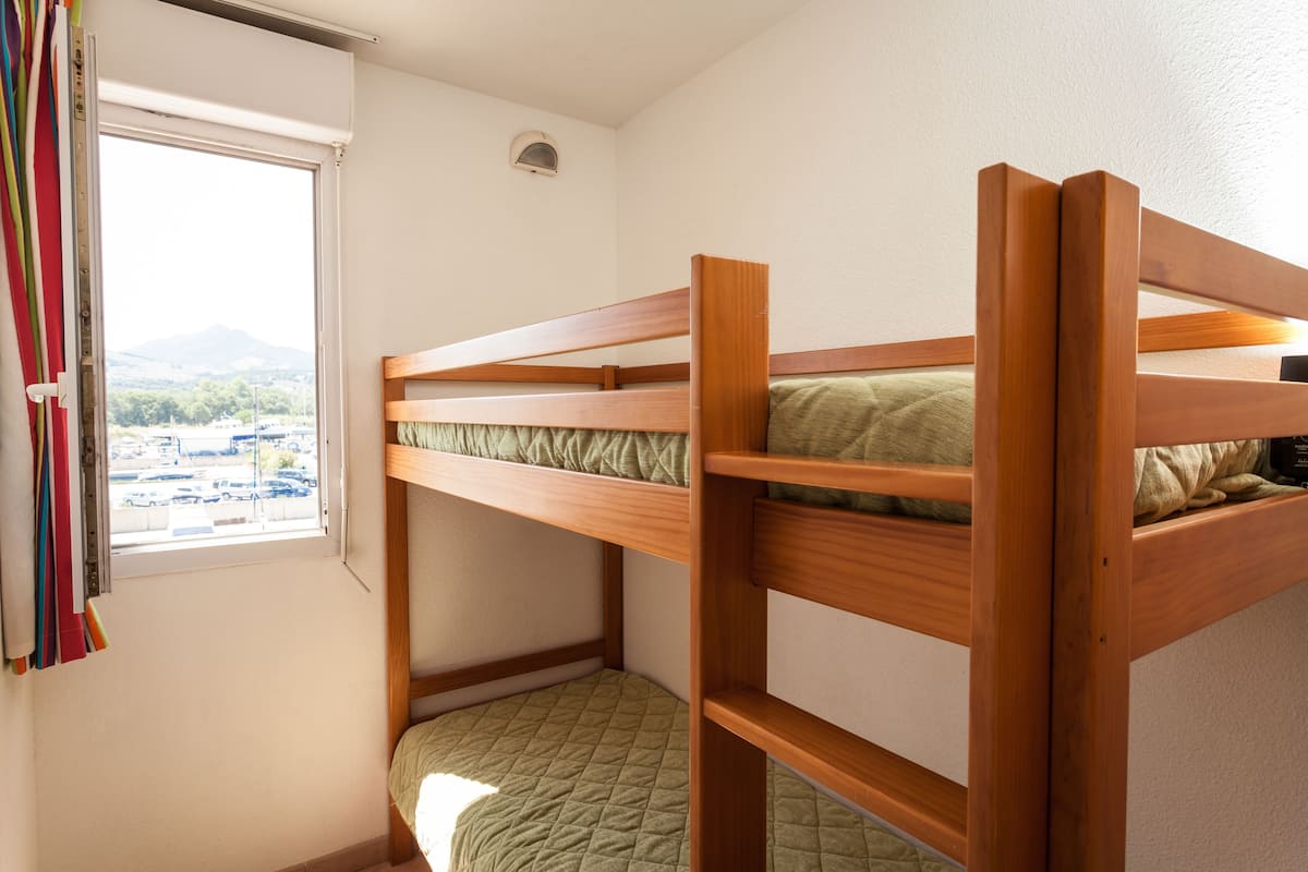 Ein Etagenbett mit Blick auf einen Parkplatz und Berge durch ein Fenster.