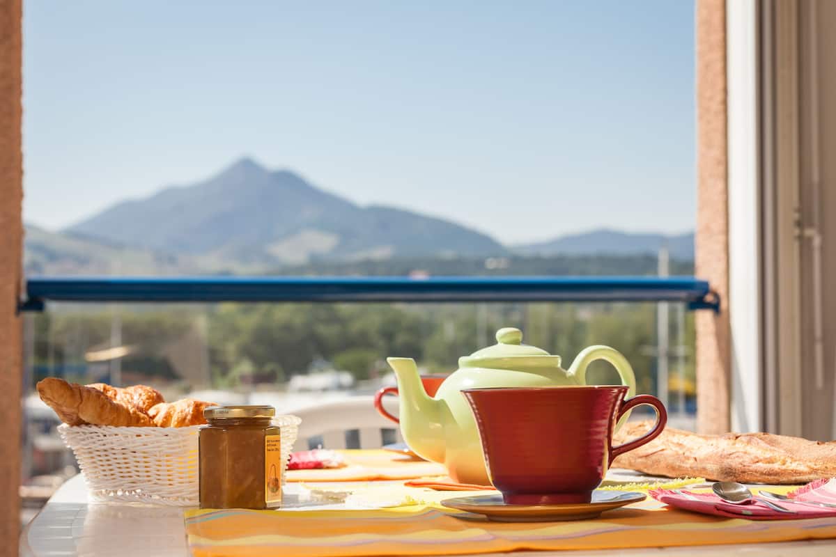 Ein Frühstückstisch mit Croissants, einem Teekessel und einer Tasse, mit Blick auf Berge.