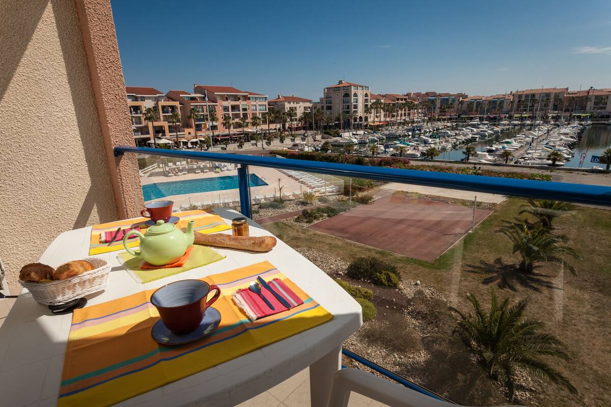 Ein Balkon mit einem Frühstückstisch, mit Blick auf eine Marina mit Booten und einem Pool.