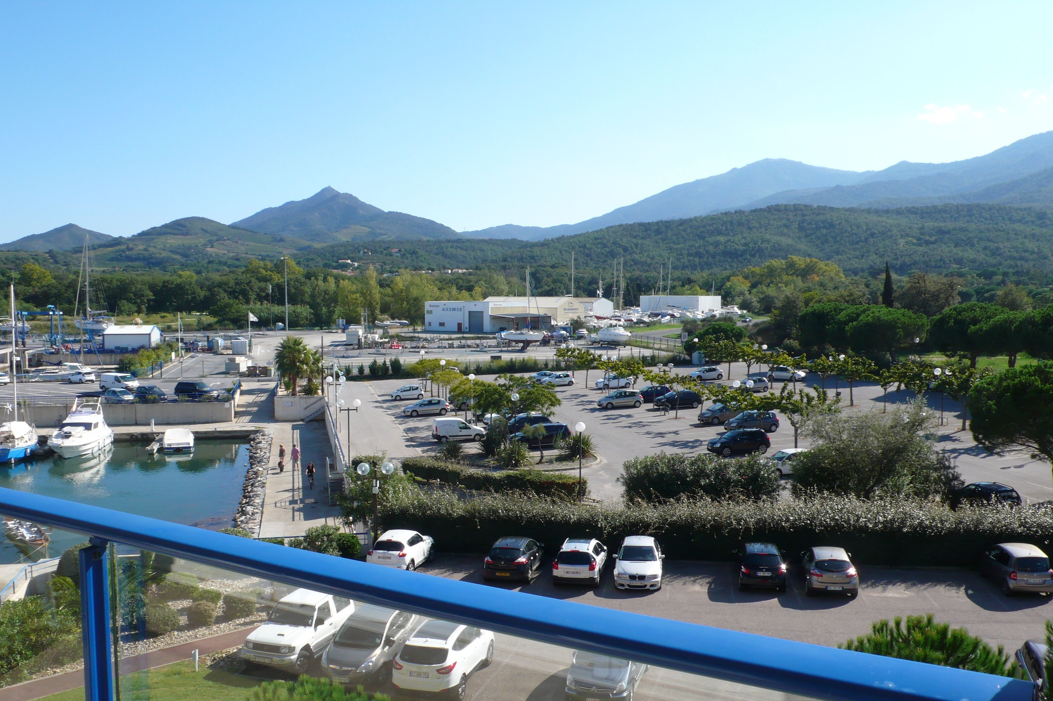 Un puerto deportivo con barcos, un estacionamiento y montañas al fondo.