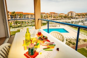 A balcony with a table set for a meal, overlooking a pool and resort buildings. - Résidence Port-Argelès (Argelès-sur-Mer)