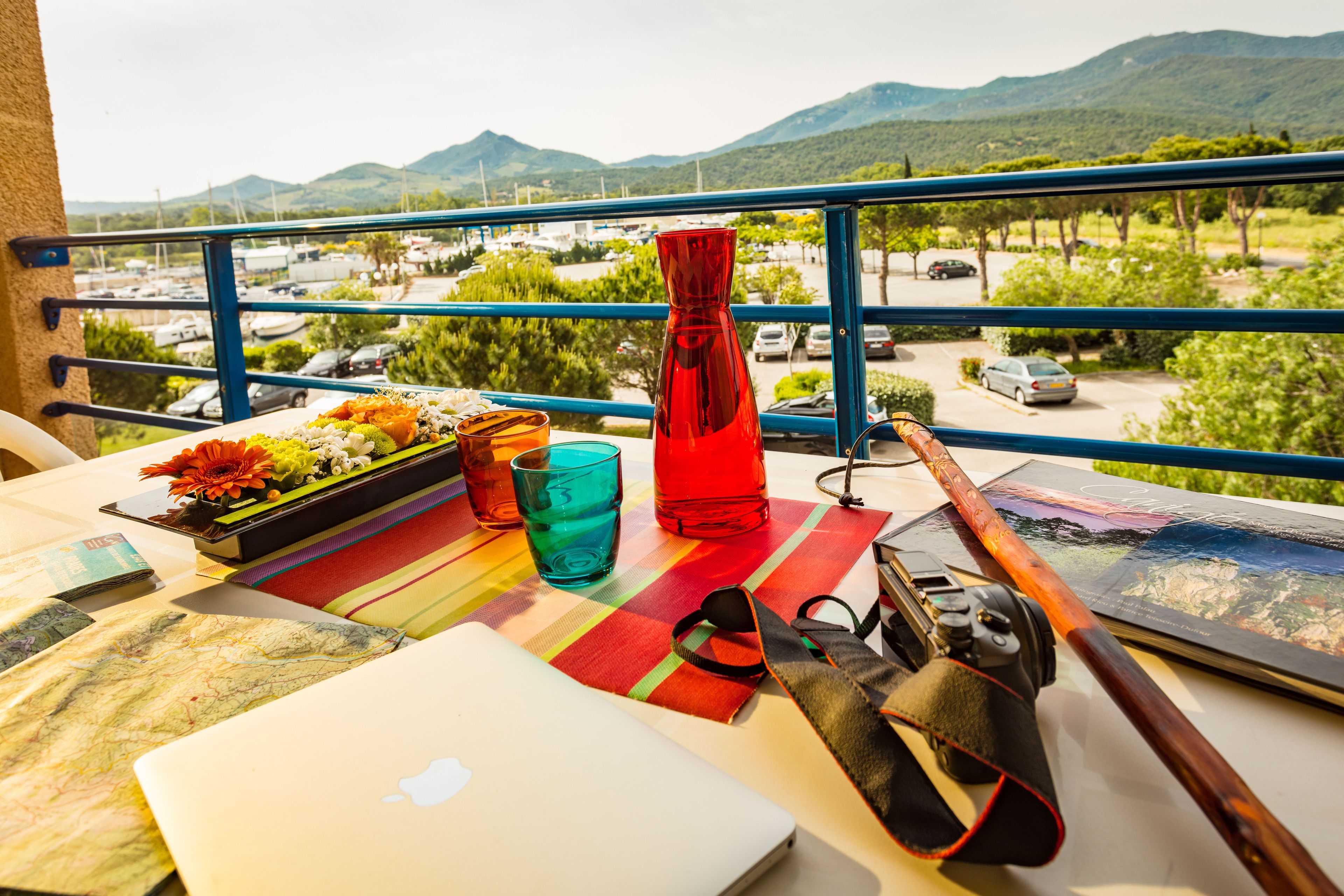 A balcony with a laptop, a camera, a red vase, and a table with a placemat.