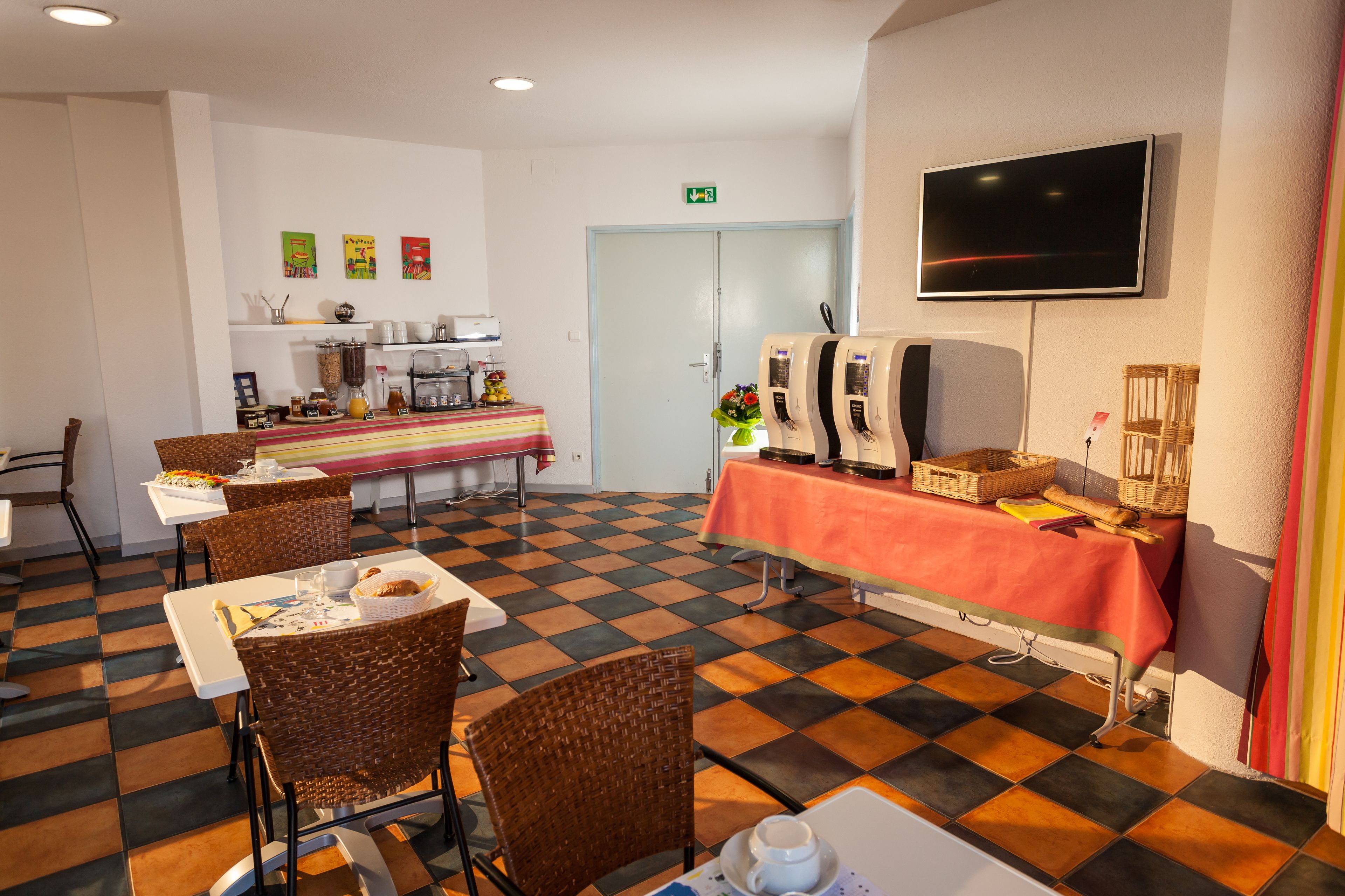 A dining area with checkered flooring, wicker chairs, a buffet table, and a television mounted on the wall.