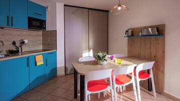 A modern kitchen with blue cabinets, a microwave, and a wooden dining table with white chairs.
