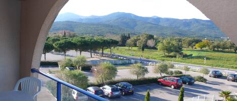 A balcony with a view of a parking lot and mountains in the distance.