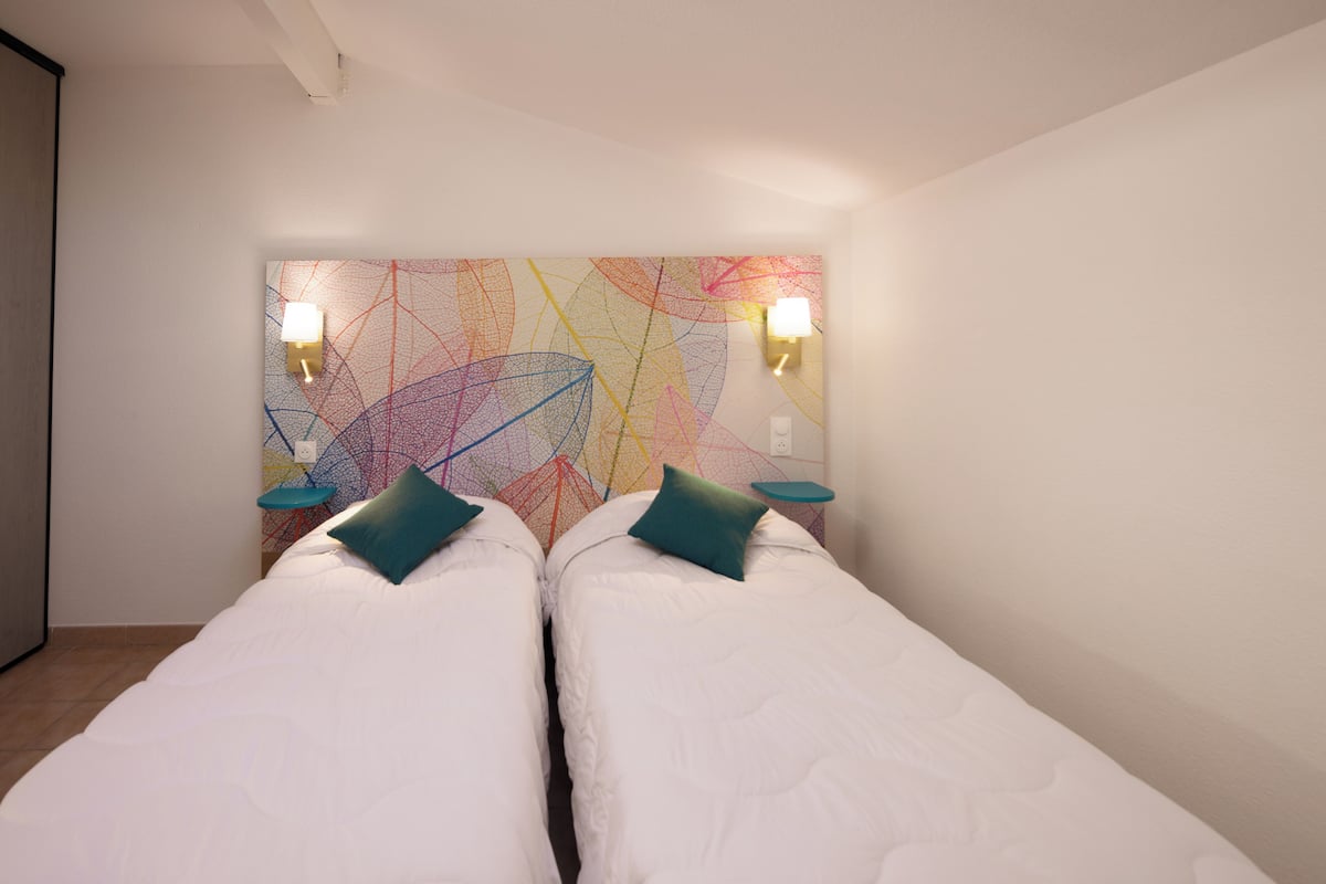 Ein Zimmer mit zwei Betten, einem farbenfrohen abstrakten Wandbild und zwei Wandleuchten.