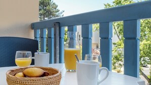 A balcony with a white table set with a basket of bread, a white mug, and glasses of orange juice. - Pierre & Vacances La Rochelle Résidence Centre (La Rochelle)