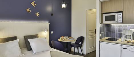 Habitació d'hotel amb un llit, una taula petita de menjador, cadires, microones i rentaplats.