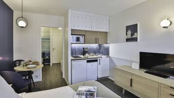 Et moderne hotelværelse med seng, spiseplads med bord og stole, et tekøkken med mikrobølgeovn, og et fjernsyn på en trækommode.
