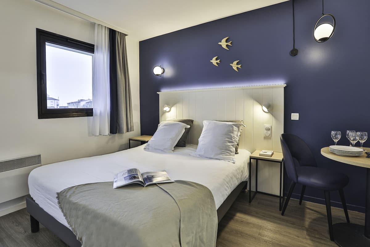 A modern hotel room with a large bed, bedside tables, a desk with a chair, and a window with curtains.
