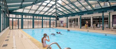 An indoor swimming pool with a glass ceiling, clear poolside area, and a lifeguard chair.