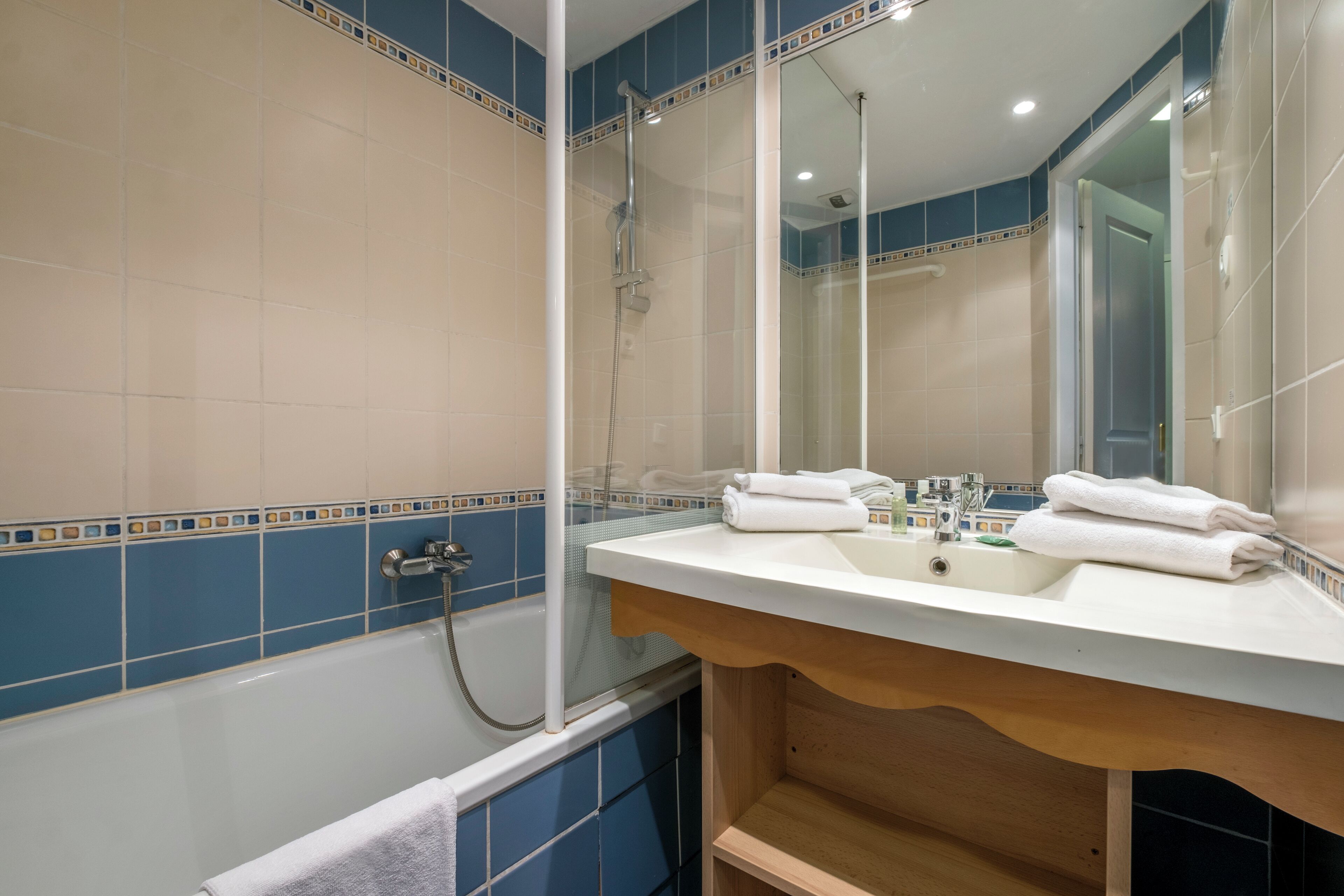 A bathroom with a bathtub, a sink with two mirrors, and blue and beige tiles.