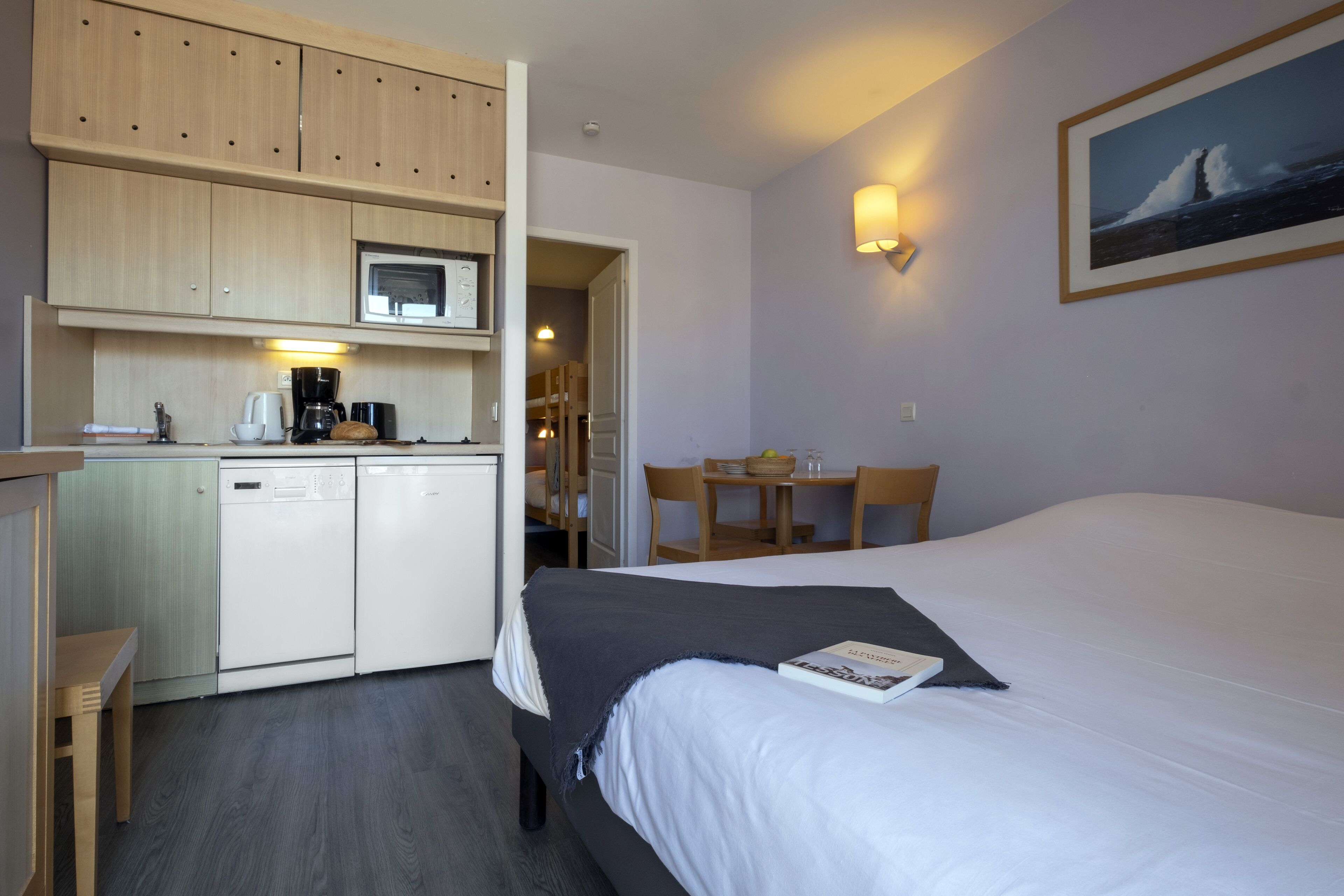 Une chambre d’hôtel compacte comprenant un coin cuisine, un lit, un espace repas et un tableau au mur.