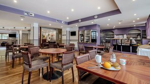 A dining area with round tables and chairs, a buffet counter, and a kitchen in the background. - Pierre & Vacances La Rochelle Résidence Centre (La Rochelle)