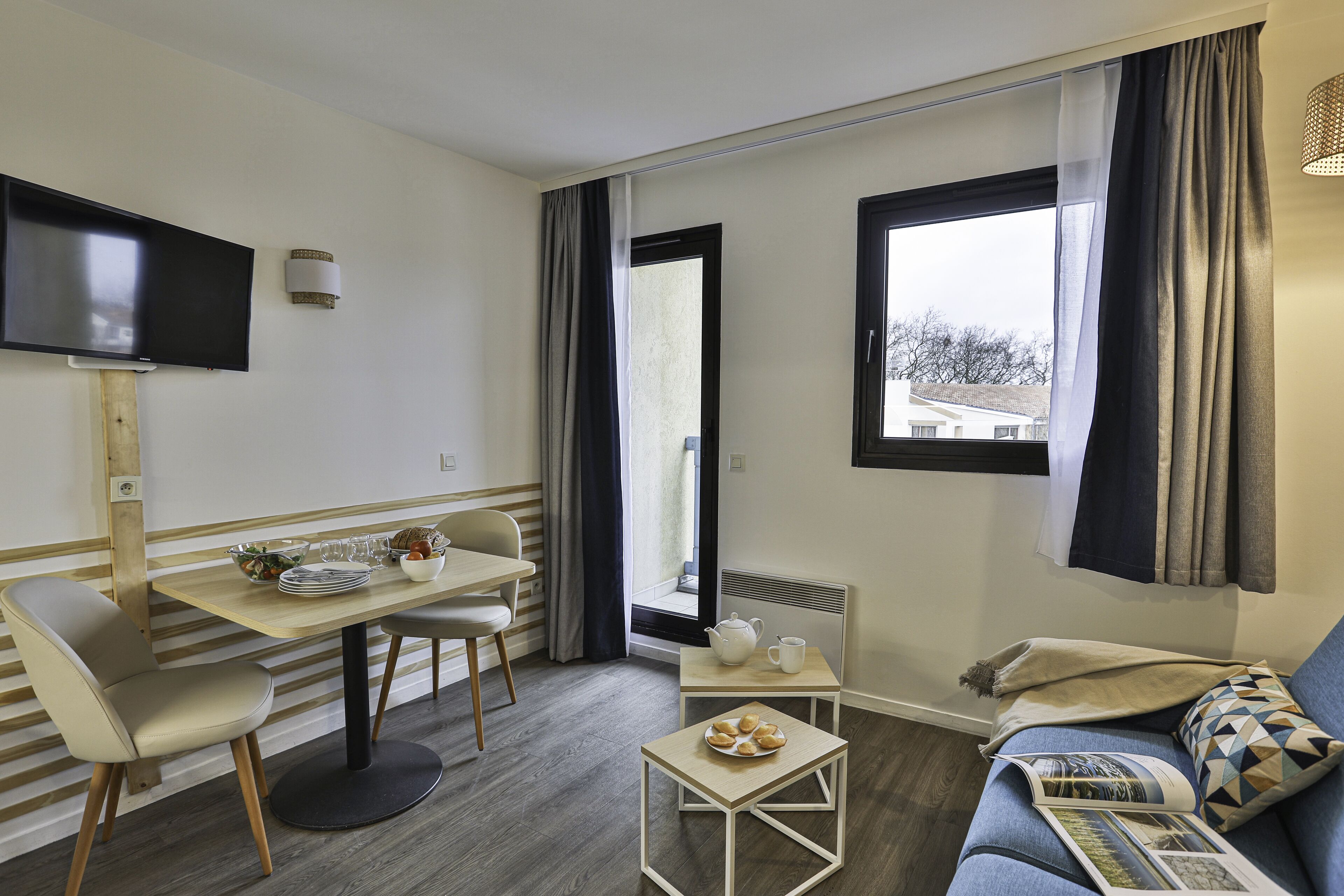 Ein modernes Wohnzimmer mit Essbereich, einem Flachbildfernseher und einem großen Fenster mit Vorhängen.