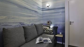 Una stanza con un divano grigio, un tavolino e una parete con un motivo astratto nei colori blu e bianco.