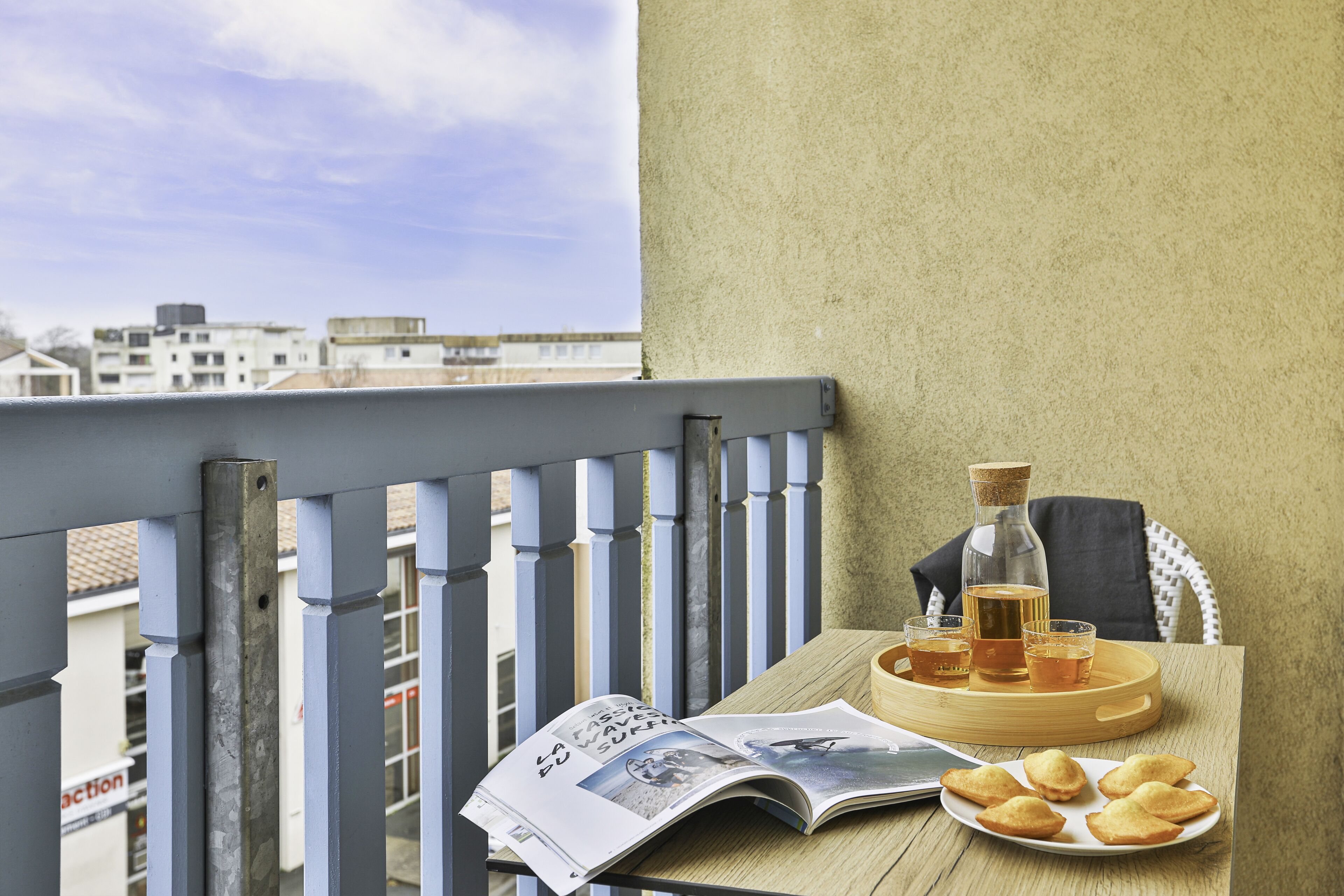 A balcony with a table set for tea, a bottle, glasses, and pastries.