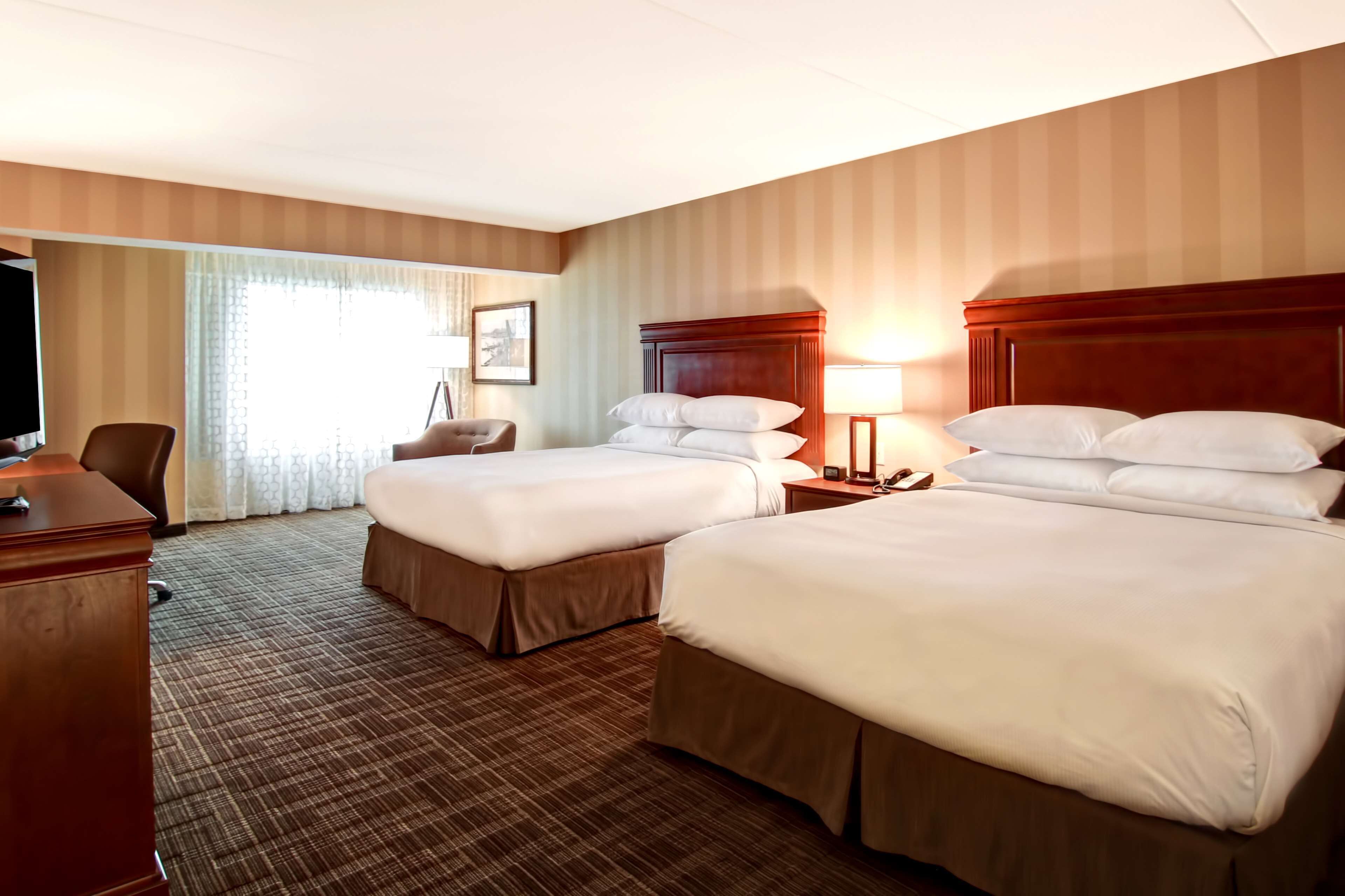 A hotel room with two beds, a desk, a chair, and a television.