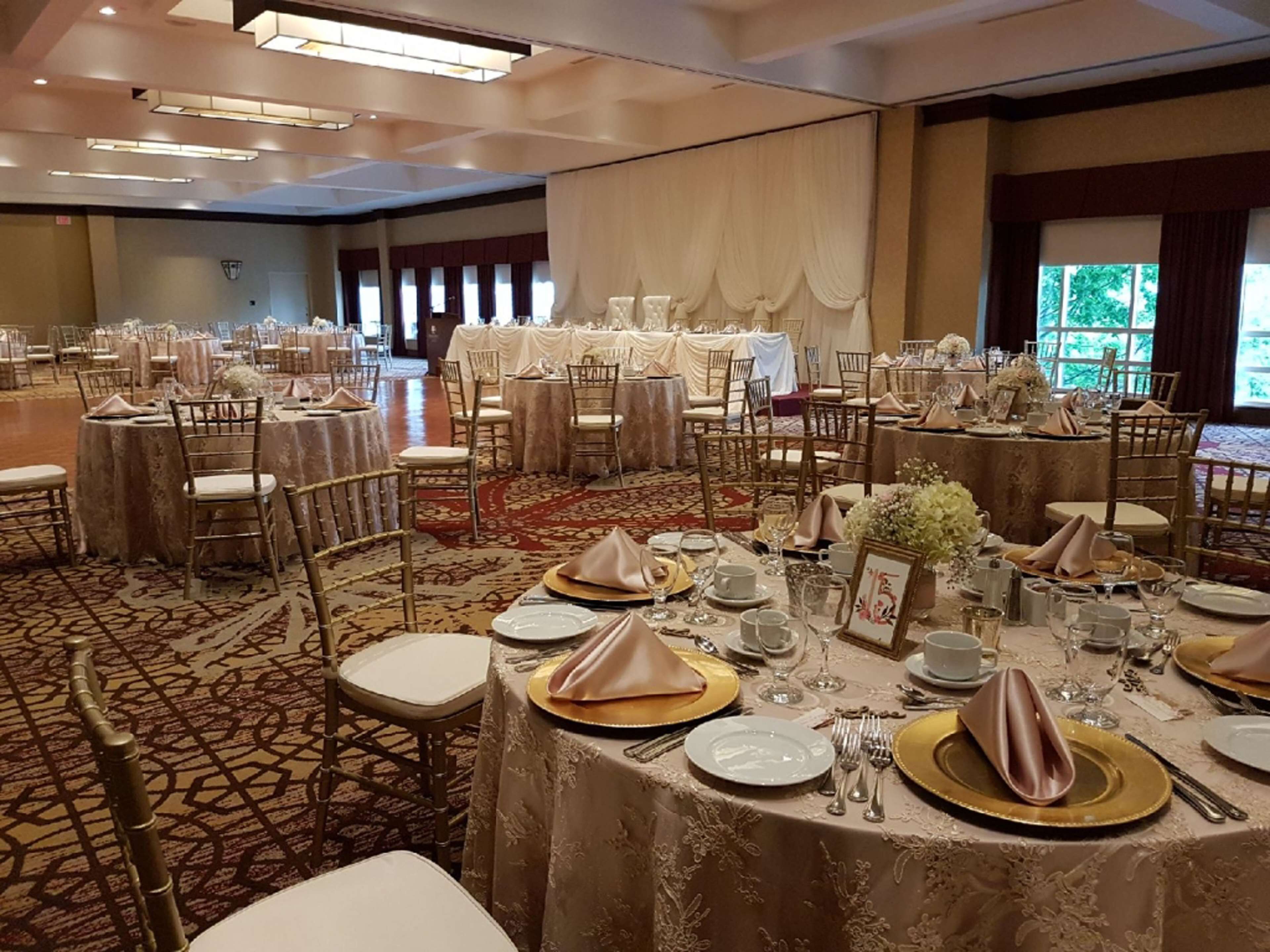 A banquet hall with round tables set for a formal event, featuring gold and white tablecloths, chairs, and a carpeted floor.