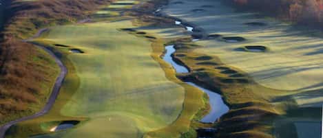 Un campo de golf con varios hoyos, obstáculos de agua y un área boscosa al fondo.