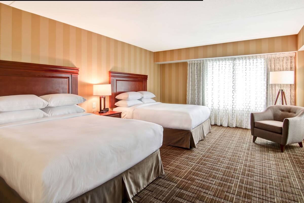 A hotel room with two beds, a chair, a lamp, and a window with curtains.