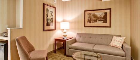 A living room with a sofa, armchair, small table, lamp, and framed pictures on the wall.