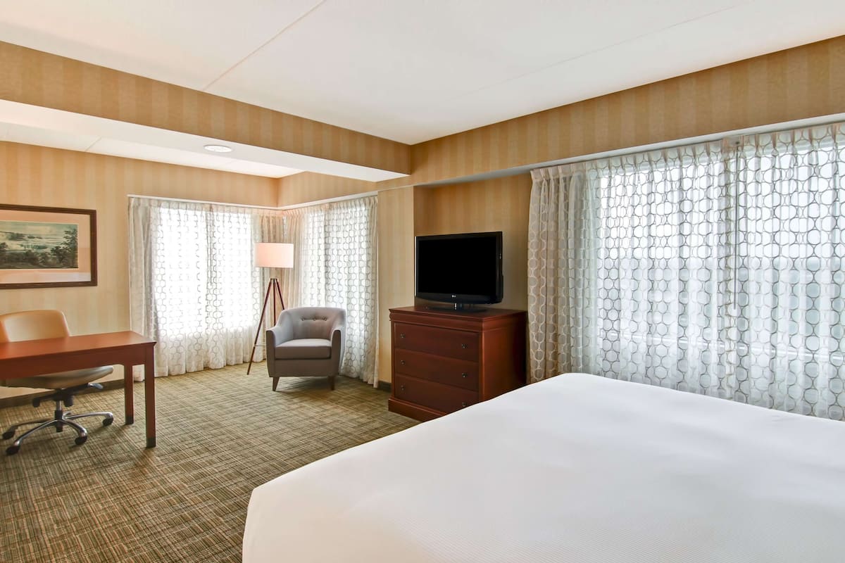 A hotel room with a large bed, a desk with a chair, a television, and a dresser.