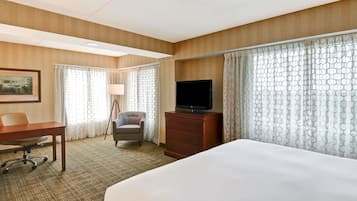 A hotel room with a large bed, a desk with a chair, a television, and a dresser.