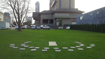 Uma área gramada com uma fileira de lajes de pedra no centro, rodeada por um edifício com telhado plano e grandes janelas.