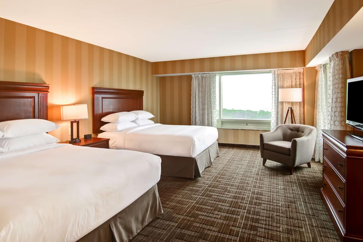 A hotel room with two beds, a chair, a TV, and a window with curtains.