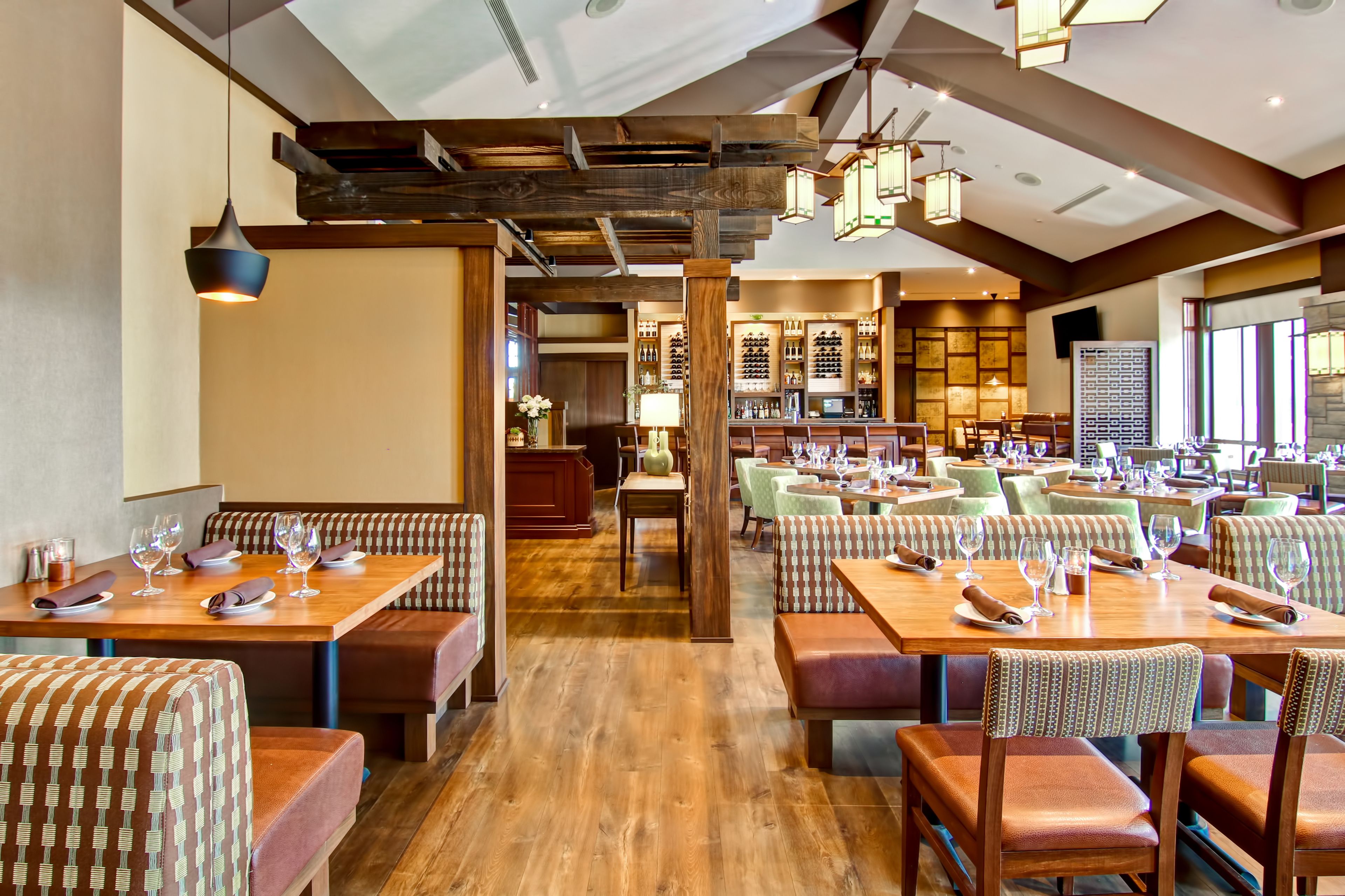 A restaurant with wooden tables and booths, a bar area, and a view of the city.