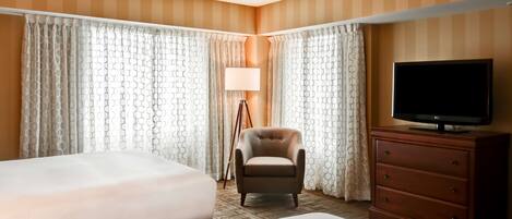 A hotel room with two beds, a chair, a TV on a dresser, and curtains with a geometric pattern.