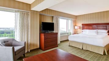 Une chambre d’hôtel avec un lit, un téléviseur posé sur une commode, une chaise et une grande fenêtre donnant sur la ville.