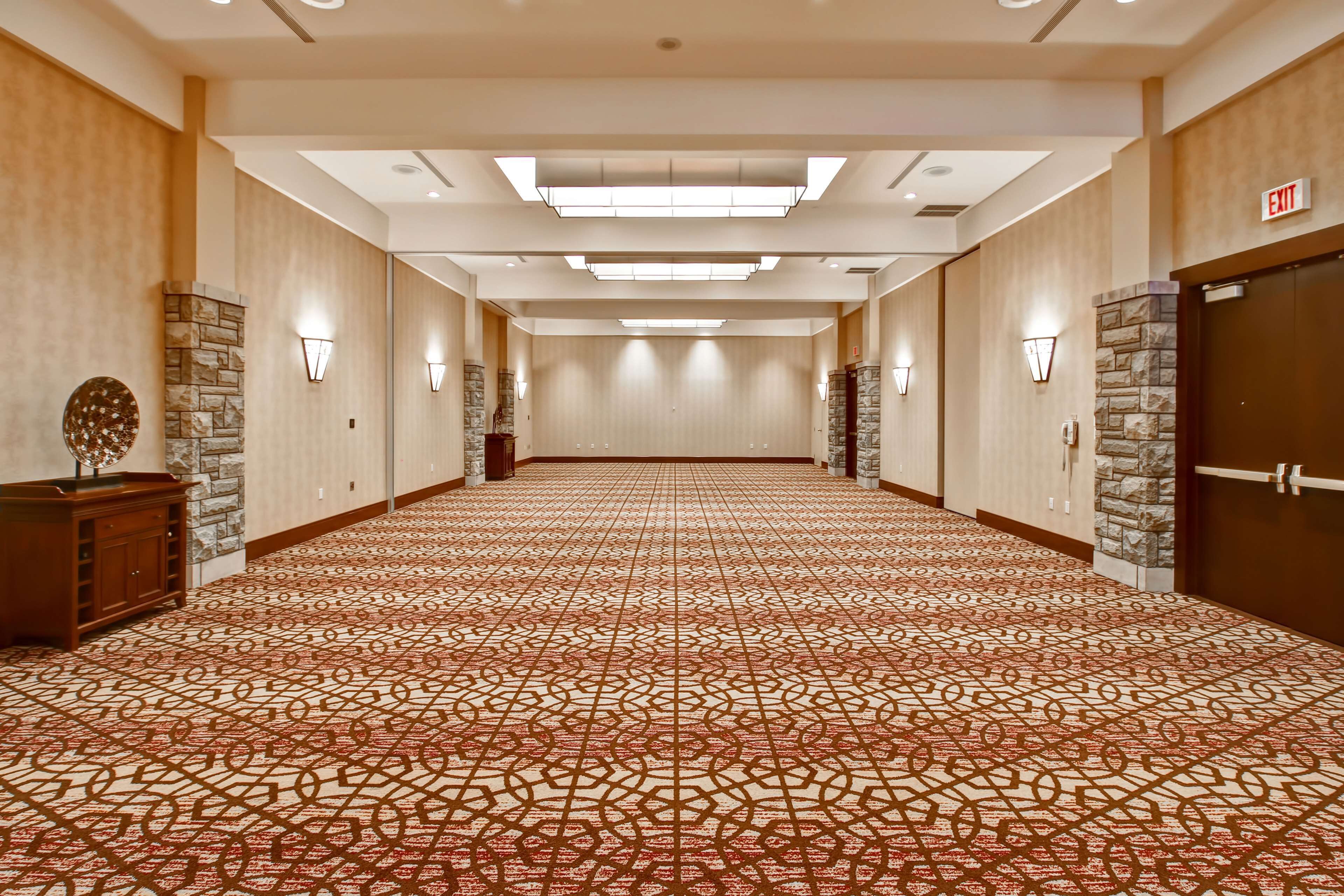 Un pasillo de hotel con alfombra estampada, detalles de piedra y apliques de pared.